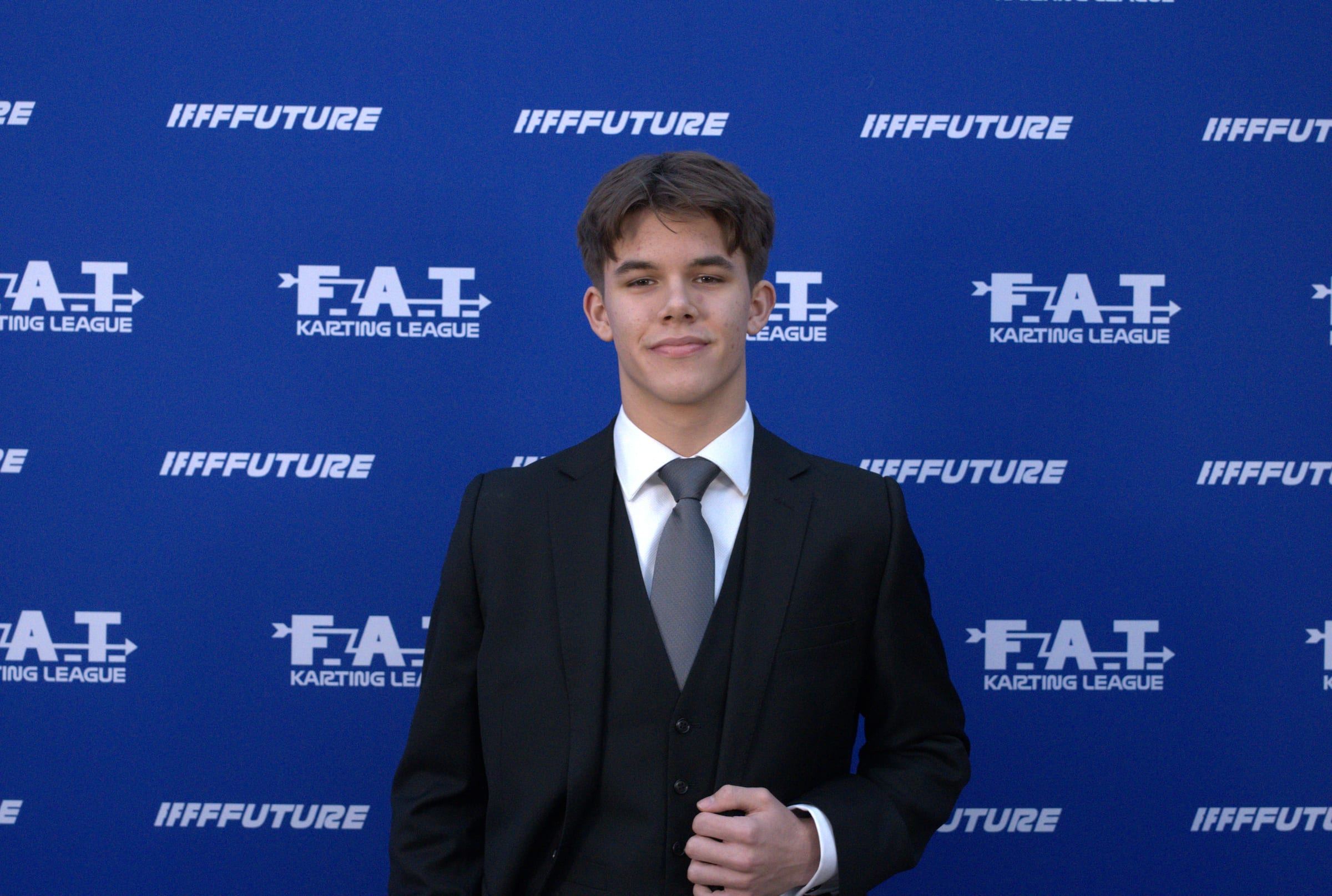 Keelan in a suit in front of the FAT Karting League press wall