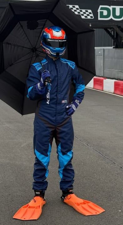 Keelan in his race suit and helmet holding an umbrella, wearing orange swimming flippers